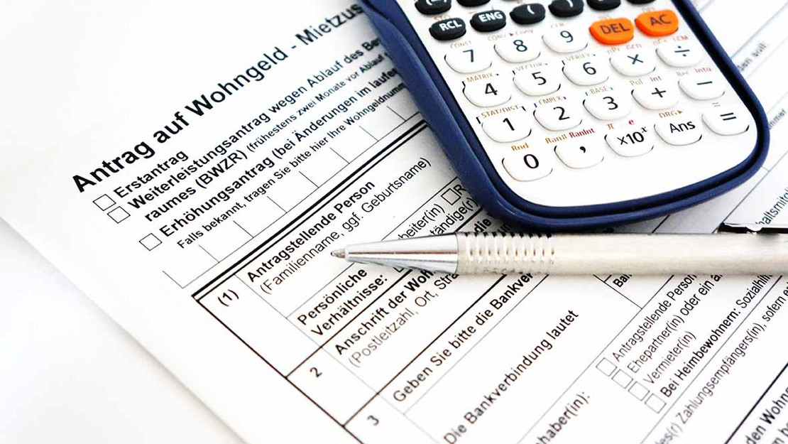 Ein Antrag für Wohngeld, auf dem ein Kugelschreiber liegt. Daneben ein Taschenrechner. 