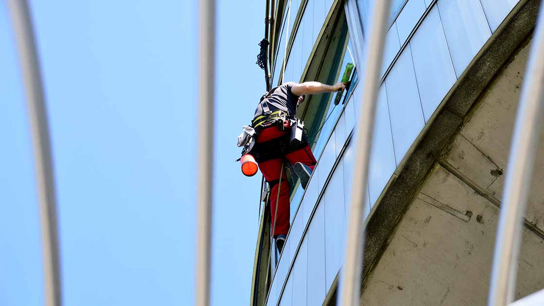Fassadenreiniger putzt Fenster an einem hohen Gebäude. 
