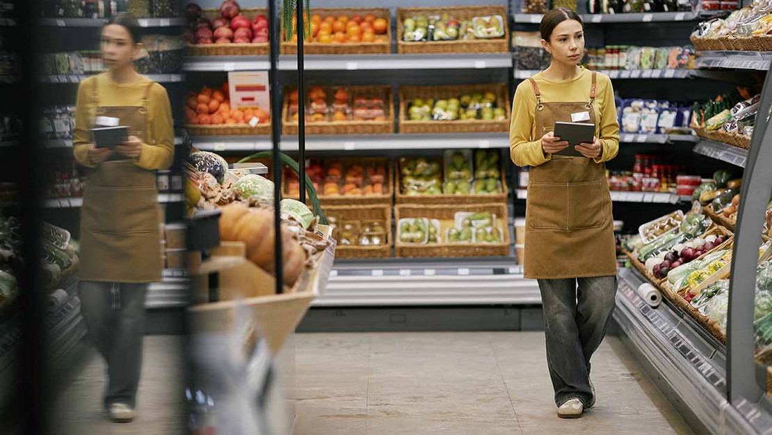 Eine junge Mitarbeiterin läuft durch die Gänge eines Supermarktes. 