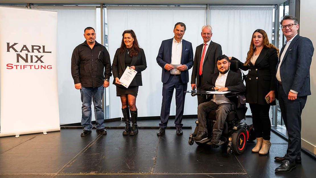 Gruppenbild mit sieben Personen, darunter ein junger Mann im Rollstuhl, der eine Urkunde in der Hand hält. 