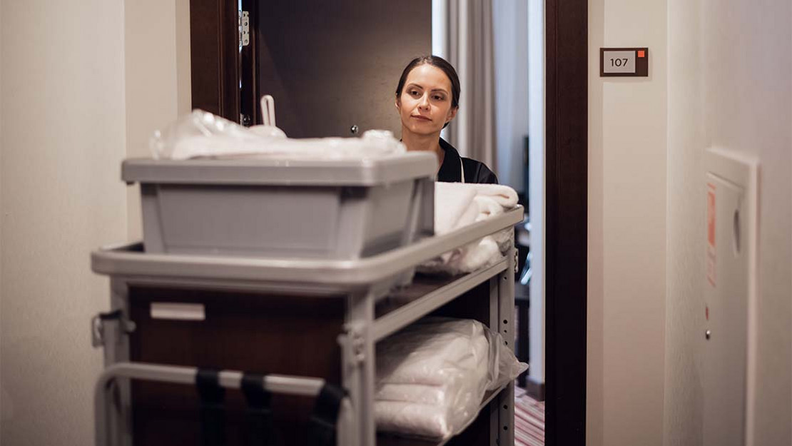Reinigungskraft schiebt einen Wagen mit Handtüchern durch den Gang eines Hotels. 
