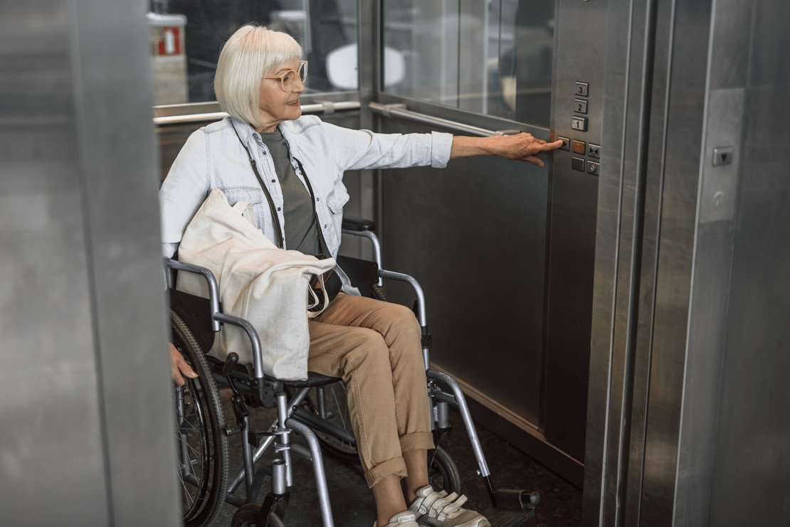 Frau im Rollstuhl nutzt einen Fahrstuhl. 