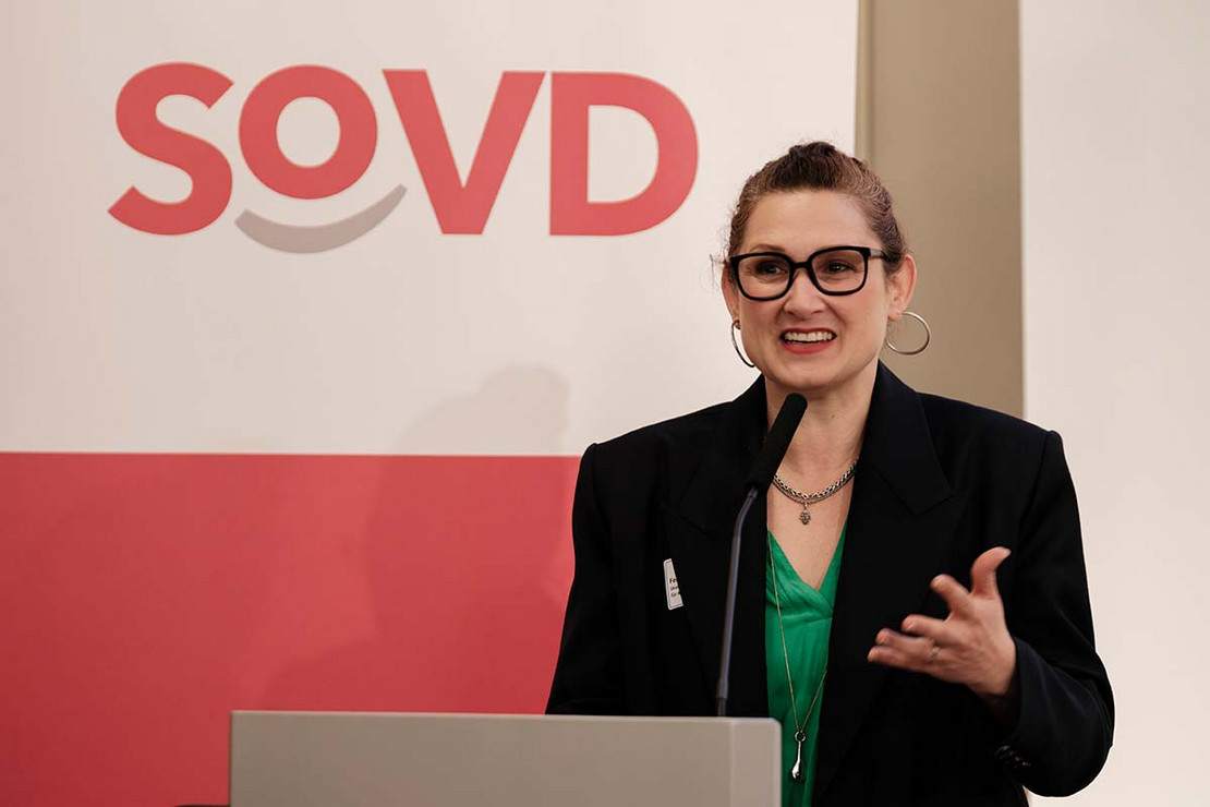 Frau steht an einem Pult, im Hintergrund das SoVD-Logo. 