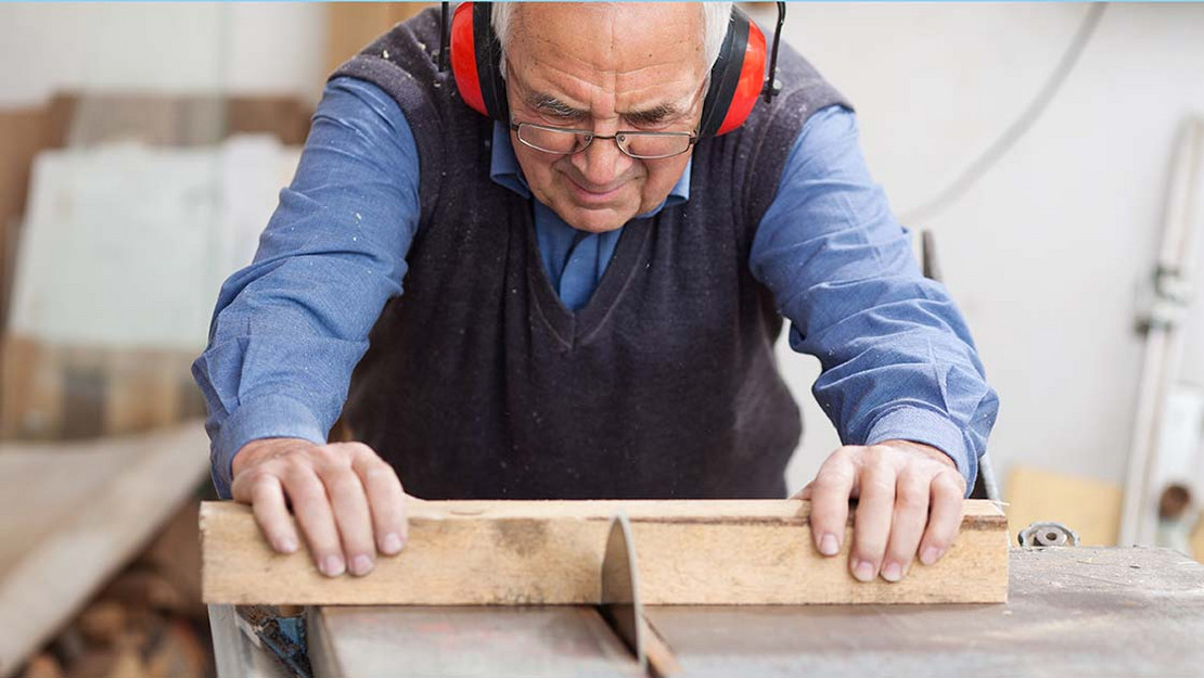 Älterer Handwerker schneidet ein Stück Holz an einer Kreissäge. 
