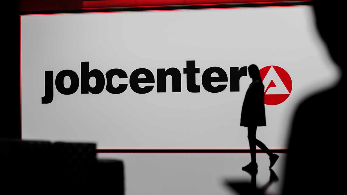 Ein großes Display mit der Aufschrift "Jobcenter" vor dem die Silhouette einer Person steht. 