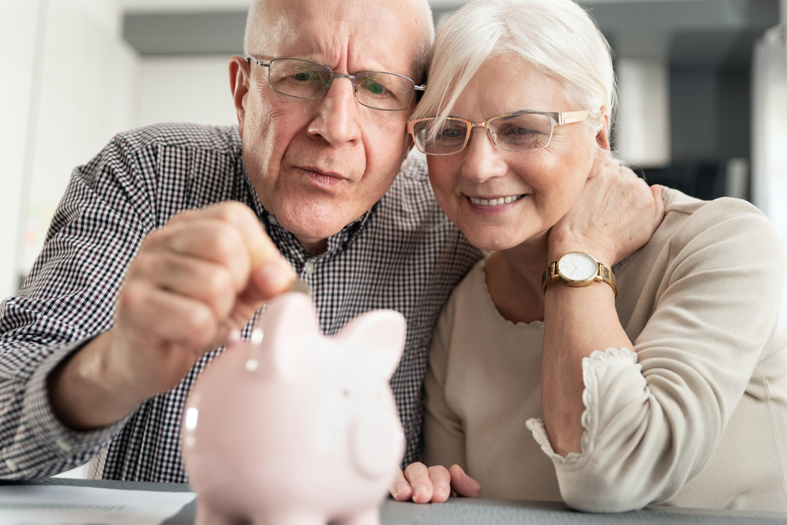 Älteres Paar steckt Geld in ein Sparschwein. 
