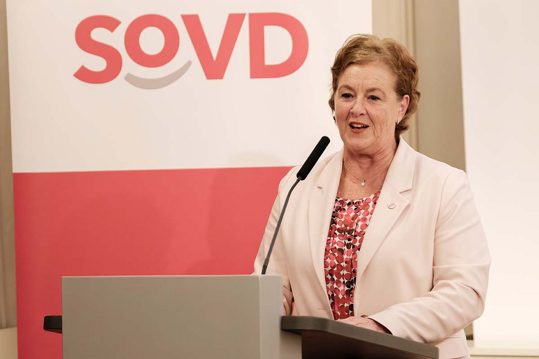 Frau steht an einem Pult, im Hintergrund das SoVD-Logo. 